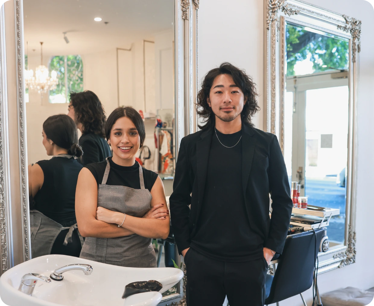 Two hairdressers posing by salon mirrors.