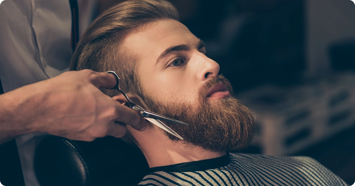 Barber trimming man's beard with scissors
